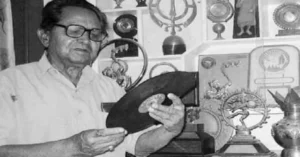 जीत सिंह नेगी एक ग्रामोफोन रिकॉर्ड हाथ में लिए सांस्कृतिक वस्तुओं के बीच दिखाई देते हुए।