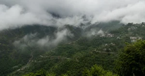Low monsoon clouds covering green Himalayan hills and settlements in Uttarakhand.