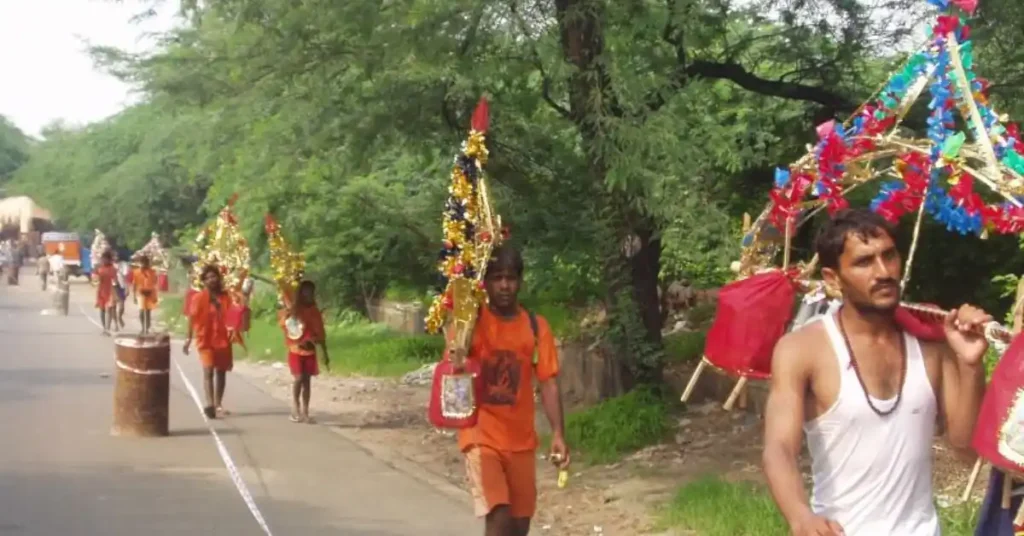Kanwariyas carrying decorated Kanwars while walking along a roadside route during the Haridwar Kanwar Yatra.