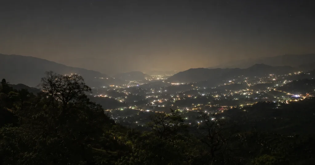 A night view of an illuminated valley in Uttarakhand where city lights outshine the natural night sky, leaving only a few stars visible.