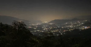 A night view of an illuminated valley in Uttarakhand where city lights outshine the natural night sky, leaving only a few stars visible.