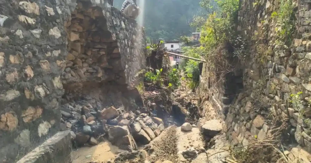A collapsed stone boundary wall inside the Narayanbagar Government Hospital campus in Chamoli after structural failure.
