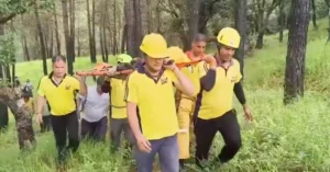 SDRF and police personnel carry a rescued young woman on a stretcher through a forest during a search operation in Ranikhet.