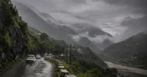 Dark monsoon clouds and rainfall over a mountain landscape in Uttarakhand.