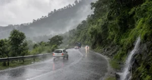 Vehicles travelling on a rain-soaked mountain road in Uttarakhand during heavy monsoon rainfall.