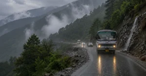 Uttarakhand Roadways bus and other vehicles travel cautiously on a rain-soaked mountain road amid low clouds and reduced visibility during the monsoon.