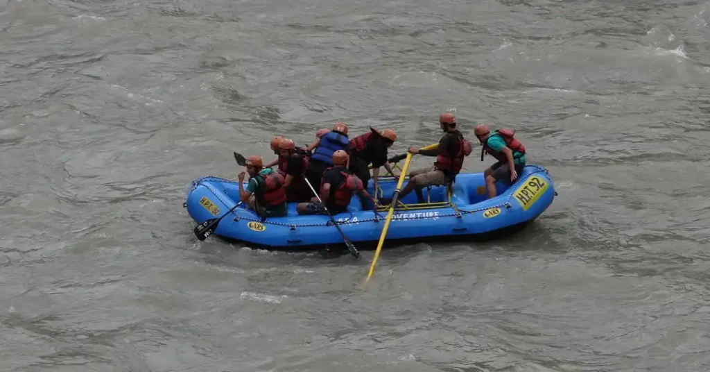 A group of tourists wearing life jackets and helmets during a guided river rafting expedition on the Ganga River in Rishikesh, Uttarakhand.