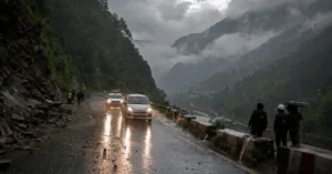 Vehicles travelling cautiously on a rain-soaked mountain road in Uttarakhand during active monsoon conditions.
