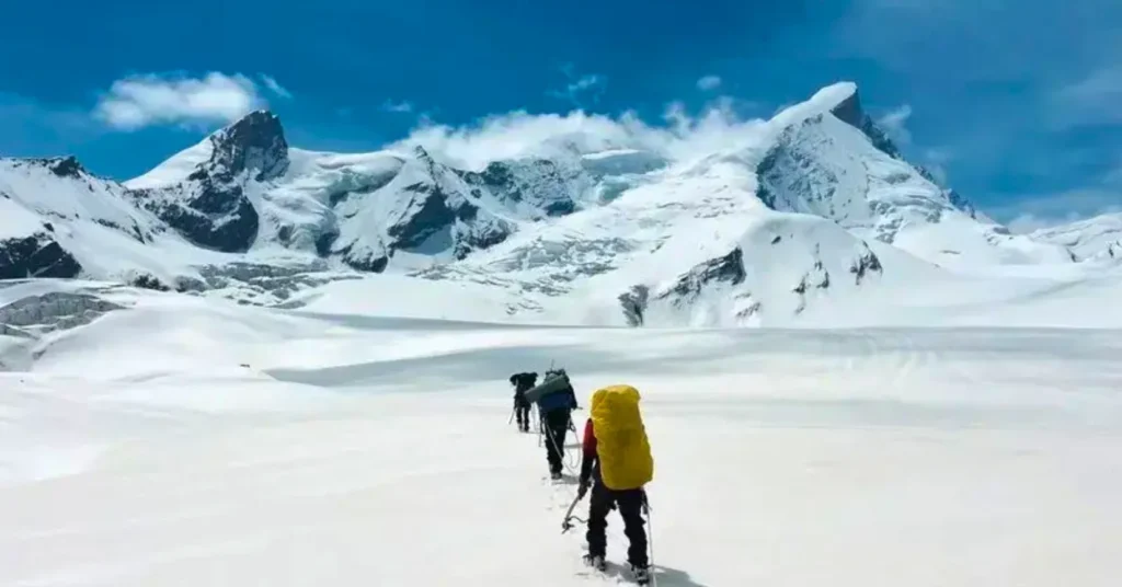 Trekkers walking across a snow-covered Himalayan glacier during a high-altitude expedition in Uttarakhand.