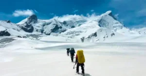 Trekkers walking across a snow-covered Himalayan glacier during a high-altitude expedition in Uttarakhand.