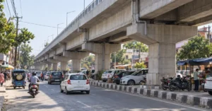 Concrete elevated corridor above a busy urban road with cars, scooters, auto-rickshaws and parked vehicles beneath the flyover.