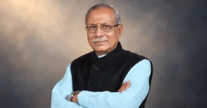 Portrait of Dr. Dhal Singh Bisen, appointed as the new Governor of Uttarakhand, wearing a black Nehru jacket over a light blue kurta with folded arms.