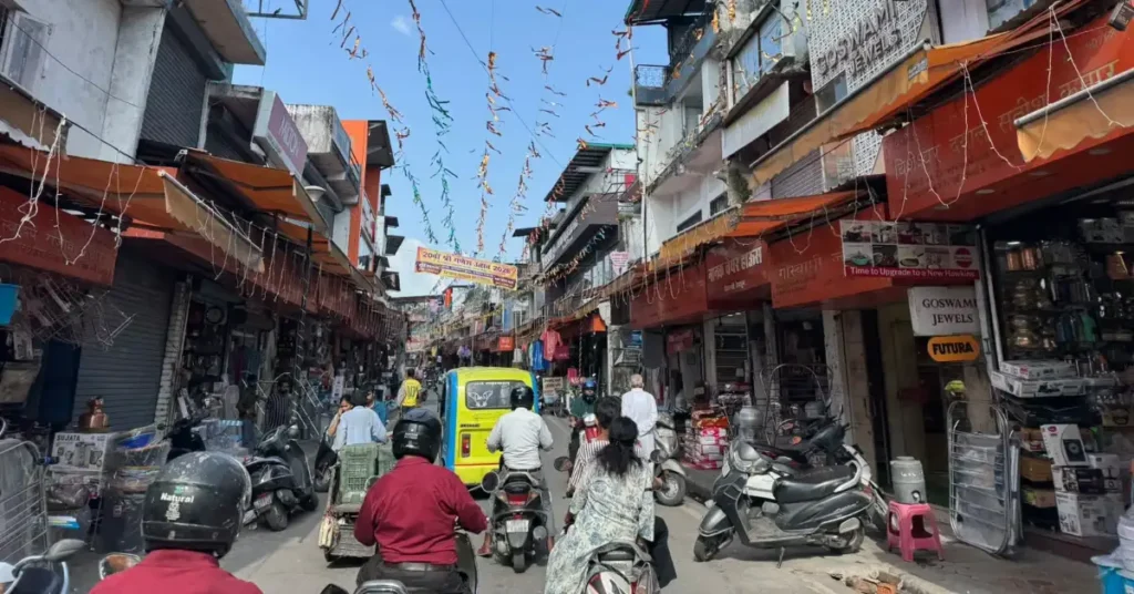 Paltan Bazaar in Dehradun showing scooters, a three-wheeler, pedestrians and shops along a busy market street.