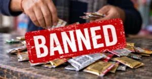 Editorial image showing small packaged sachets on a shop counter with a prominent red BANNED graphic, representing Uttarakhand's ban on gutkha and tobacco-nicotine-containing pan masala.